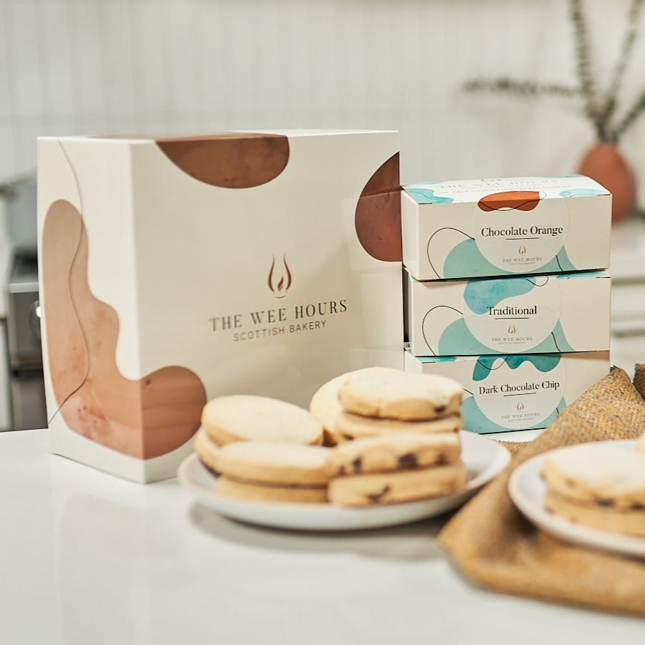Shortbread cookies on two plates in front of The Wee Hours Scottish Bakery gift box, on a white surface.