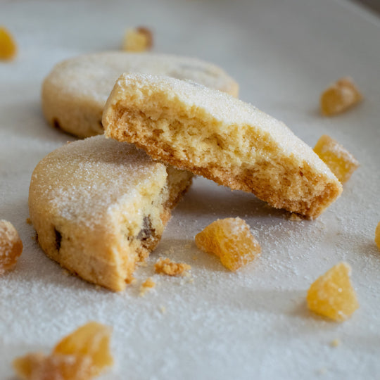 A stem ginger shortbread cookie split in two with one half sitting on top of the other with a dusting of sugar on them, on a white background.