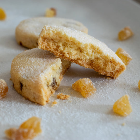 A gluten free stem ginger shortbread cookie split in two with one half sitting on top of the other with a dusting of sugar on them, on a white background.