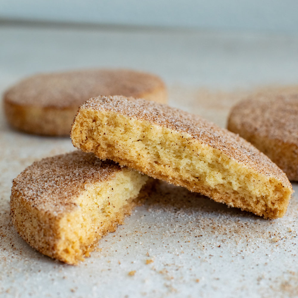 A cinnamon shortbread cookie split in two with one half sitting on top of the other with a dusting of cinnamon sugar on them, on a white background.