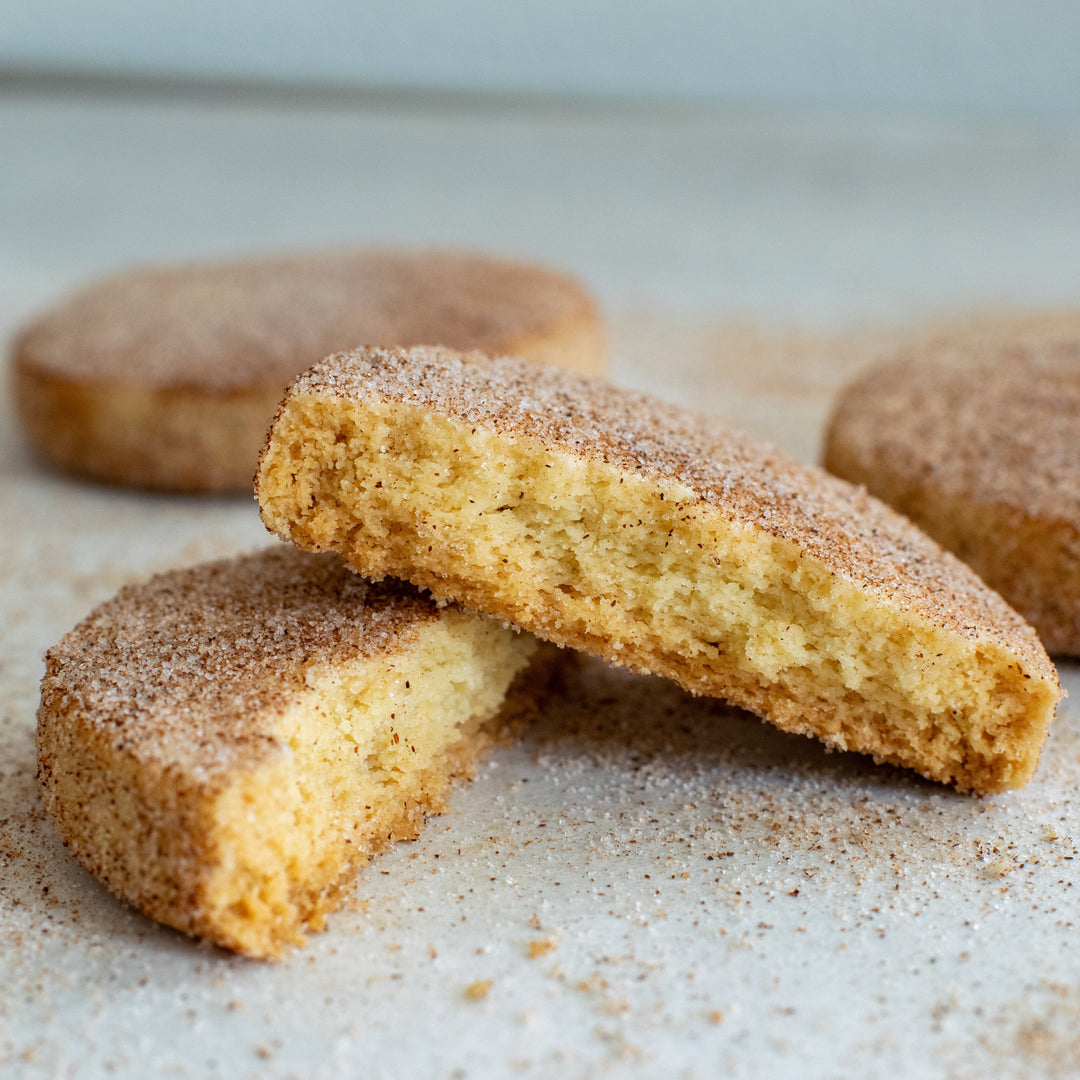 A cinnamon shortbread cookie split in two with one half sitting on top of the other with a dusting of cinnamon sugar on them, on a white background.