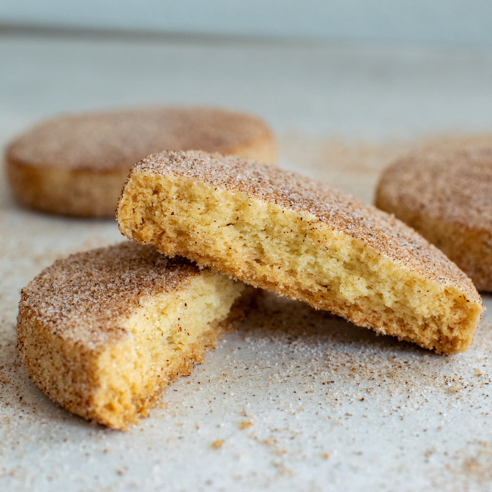 A gluten free cinnamon shortbread cookie split in two with one half sitting on top of the other with a dusting of cinnamon sugar on them, on a white background.