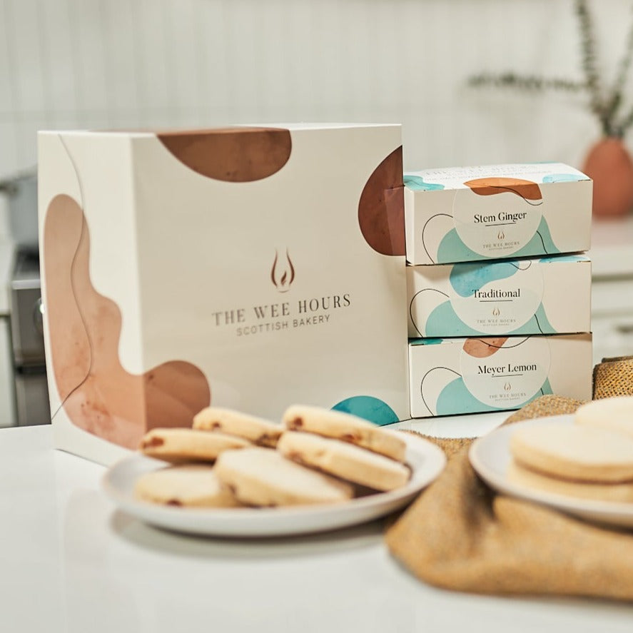 Shortbread cookies on two plates in front of The Wee Hours Scottish Bakery gift box, on a white surface.